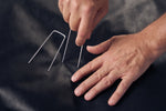 Hands pressing U-shaped metal landscape pins into black landscaping fabric, showing installation use.