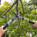 Expert Gardener loppers cutting a thick tree branch, photographed outdoors among green foliage.
