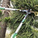 Extendable lopper cutting a branch in a tree, shown in-use among green foliage