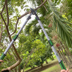 Lopper held open above a garden, showing full length handles with green grip accents and blade at top