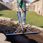 Person using an Expert Gardener landscaping rake to smooth soil at a garden bed edge in a residential yard