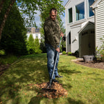 Person using an Expert Gardener leaf rake on a lawn beside a house, collecting a pile of leaves