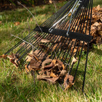 Close detail of rake tines lifting dry leaves and small twigs from grass, showing metal construction