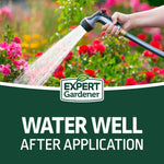 Hand holding a watering wand spraying water over flowering plants above the Expert Gardener logo and watering instruction text