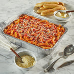 Aluminum disposable baking pan filled with pasta and grated cheese on a marble table