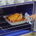 Aluminum roaster pan with roasted chicken and vegetables being placed into an oven using a cloth
