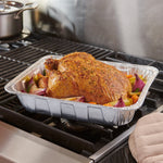 Aluminum roaster pan on stovetop grill with a seasoned roasted chicken and vegetables inside