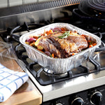 Roast beef with vegetables in an aluminum disposable roasting pan sitting on a gas stove with a clear lid nearby