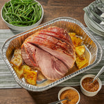 Cooked ham and roasted pineapple served in an EZ Foil disposable aluminum roasting pan on a tabletop with sides and plates nearby.