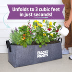 Gray fabric raised bed holding flowering plants and tomatoes with a banner reading 'Unfolds to 3 cubic feet in just seconds!'