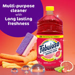 Red Fabuloso cleaner bottle with cleaning sponge, cloths and citrus slices on orange gradient background.