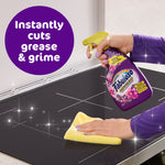 Hand spraying Fabuloso lavender multi-purpose cleaner while another hand wipes a stovetop with a yellow cloth