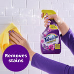 Hand holding Fabuloso lavender spray bottle while wiping white tile backsplash with a yellow cloth