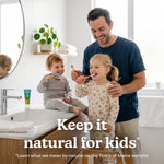 Smiling adult with two young children brushing teeth at a bathroom sink, Tom’s toothpaste tube visible on the counter and overlay text Keep it natural for kids.