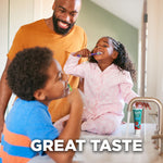 Lifestyle photo of smiling children and an adult brushing teeth at a bathroom sink with a Tom's of Maine kids toothpaste tube visible on the counter.