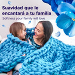 Adult and child wrapped in a chunky blue knit blanket with blue flowers and text about softness in Spanish and English