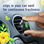 Hand pinching a Febreze AUTO vent clip as it is being clipped into a round car vent, floral graphics at edges