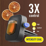 Close-up product render of a Febreze AUTO vent clip with intensity dial graphic and dried orange slices on wood background