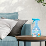 Febreze Fabric spray bottle placed on a wooden side table next to sofa cushions