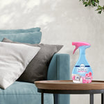 Febreze FABRIC Downy April Fresh bottle placed on a wooden side table beside a teal sofa and pillows.