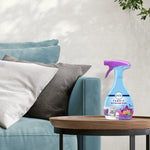 Styled home scene with a Febreze Fabric Gain Moonlight Breeze bottle placed on a round wooden side table near a couch.