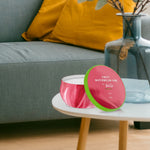 Lifestyle photo of Febreze Sweet Watermelon Vine tin candle on a small round table beside a sofa and decorative vase