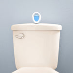 Lifestyle image of a Febreze Small Spaces oval device sitting on top of a toilet tank against a pale blue wall