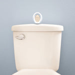 Febreze oval bathroom air freshener device sitting on top of a toilet tank against a pale blue wall