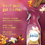 Close-up of a pink-purple Febreze Luxe spray bottle with floral and vanilla imagery and text highlighting fresher scent and longer-lasting sprays.