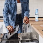 Lifestyle shot of a person recycling a plastic bottle with a Febreze Air Mist bottle visible on the kitchen counter.
