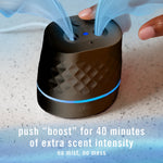Black Febreze PLUG device on a counter with blue indicator light and finger pressing a boost button releasing scent visuals