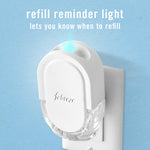 White Febreze plug-in air freshener inserted in an outlet with a glowing refill reminder light and blue wall