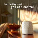 Febreze Plug scent booster device placed on a wooden table in a warmly lit room with text 'long-lasting scent you can control'.