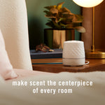 Febreze Plug Scent Booster placed on a bedside or side table in a styled room with text about making scent the centerpiece