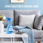 Febreze fabric spray bottle staged on a coffee table in a living room scene with couch and throw blanket
