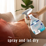 Hand holding and spraying a Febreze Fabric Heavy Duty bottle onto an orange decorative pillow on a sofa.