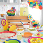 Colorful party table scene with bowls, plates, balloons and multicolor plastic forks used as part of a fiesta setup.