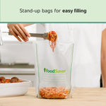 Person using tongs to fill a FoodSaver stand-up vacuum bag with spaghetti on a kitchen counter