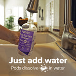 Hand holding a Podsy multi-surface cleaner bottle under a kitchen faucet filling it with water