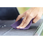 Fingers holding and using a purple abrasive pad to scrub grill grates in a close-up action shot