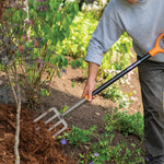 Gardener using a Fiskars fiberglass-handled pitchfork to turn mulch in a planted garden bed.