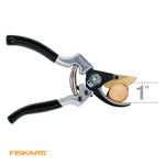 Fiskars pruner cutting a small wood cross-section with a 1-inch size indicator, on white background.