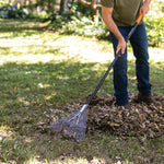 Person using a Fiskars metal-tine leaf rake to gather a pile of leaves on a grassy yard.