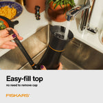 Person filling a Fiskars watering can at a kitchen sink, demonstrating the easy-fill top in use