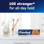 Fixodent Ultra package on a bathroom counter with toothbrushes and headline claiming 10X stronger