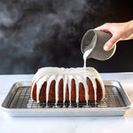 Iced fluted loaf cake on a cooling rack with glaze being poured from a small pitcher over the top
