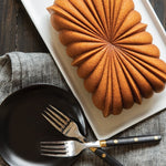 Brown fluted loaf cake with a radiating starburst pattern served on a rectangular white platter beside forks