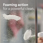 Close-up of foaming cleaner on a glass shower door with text "Foaming action for a powerful clean."
