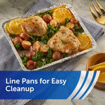 Aluminum foil-lined disposable pan holding roasted chicken thighs, potatoes, kale, and lemon slices.