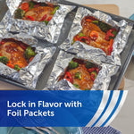 Four foil packets on a baking sheet holding glazed chicken and vegetables, top-down cooking shot